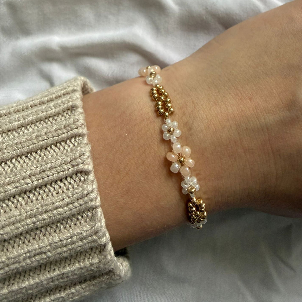 Perlenarmband mit weißen und beigen Blumen und goldenen Verzierung