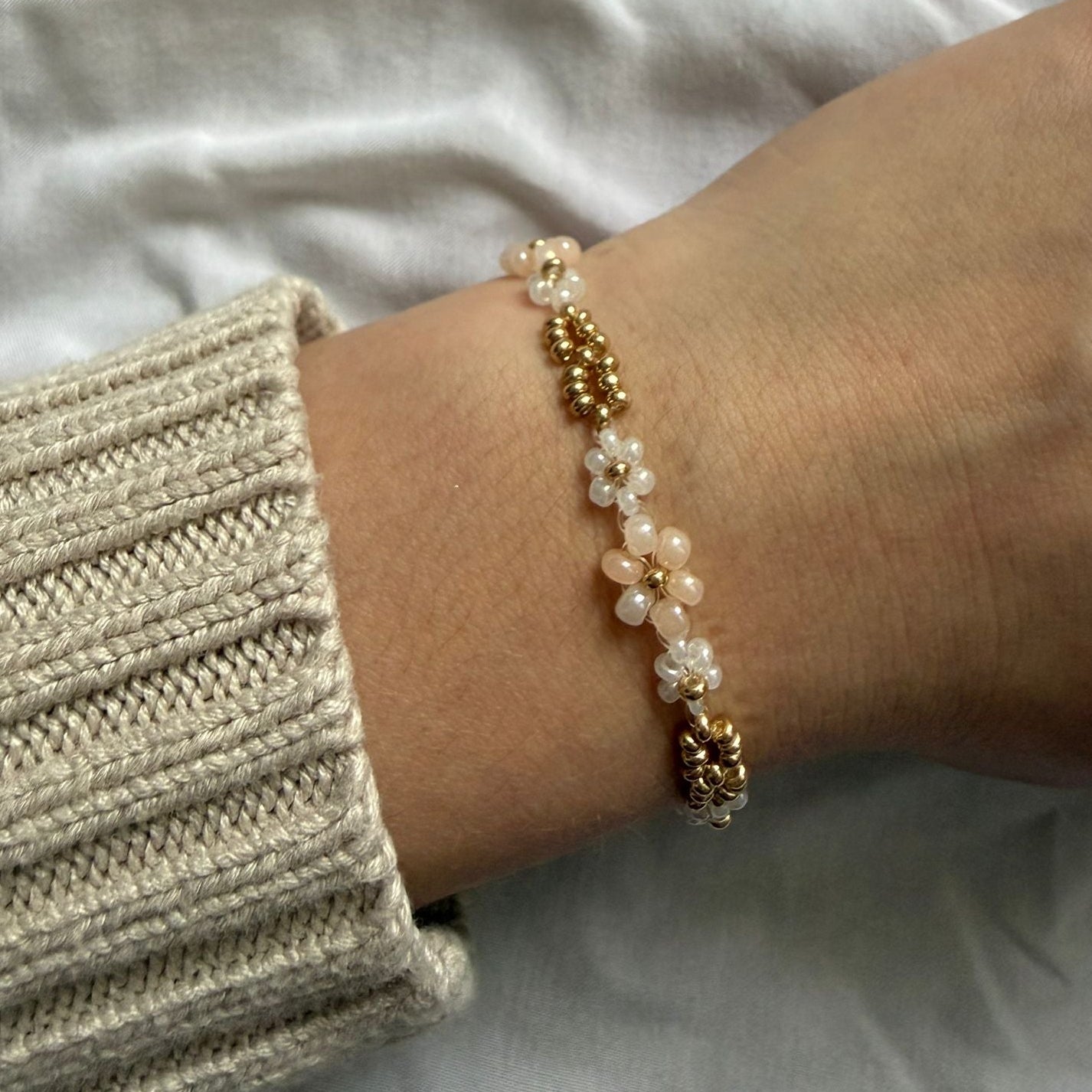 Perlenarmband mit weißen und beigen Blumen und goldenen Verzierung
