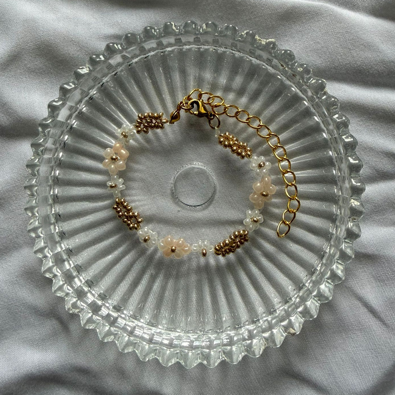 Perlenarmband mit weißen und beigen Blumen und goldenen Verzierung